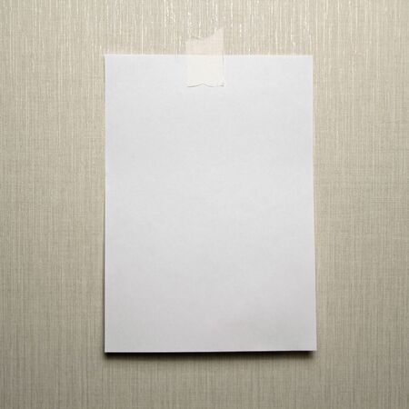 A4 white sheet of paper hanging on a wall glued with a piece of paper tape on a light background.の写真素材