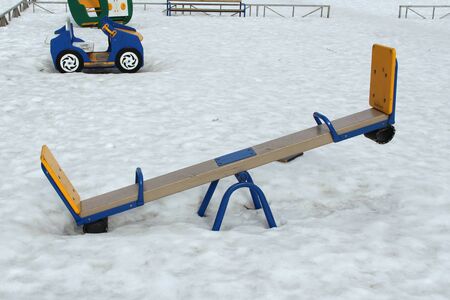 Childrens swing for two on the playground against the background of winter snowdrifts. Concept of childrens entertainment and street games. Stock photo for web and print with empty space for text.の写真素材