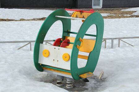 Childrens swing in the form of a car on the playground against the background of winter snowdrifts. Concept of childrens entertainment and street games. Stock photo for web and print with empty space for text.の写真素材