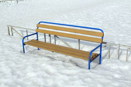 Wooden light bench with a metal blue base on a snow background. City landscape, recreation area. Stock photo for web and print.の写真素材