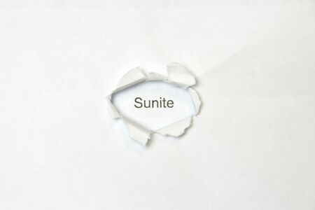 Word sunite on white isolated background, the inscription through the wound hole in the paper. Stock photo for web and print with empty space for text and design.の写真素材