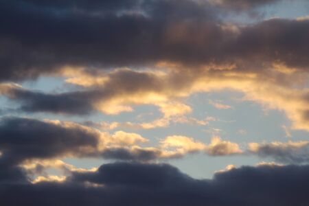 Clouds in the blue sky at sunset or dawn backlit by the sun. Place for text and design.