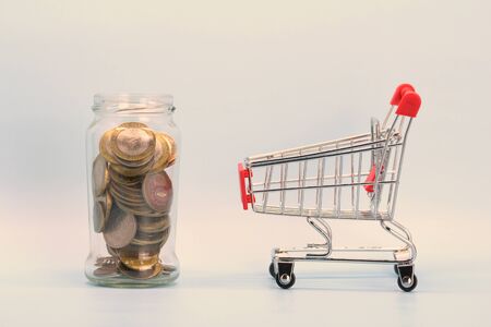 Shopping cart and glass transparent jar with Russian money. Metal coins and a souvenir shopping basket.の写真素材