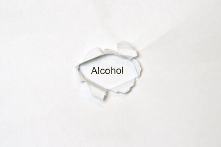 Word alcohol on white isolated background, the inscription through the wound hole in the paper. Stock photo for web and print with empty space for text and design.の写真素材