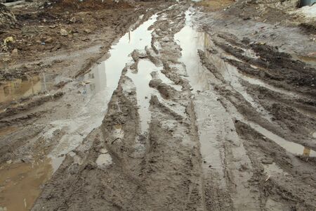 Dirty dirt road with track, wheel marks, brown clay and puddles in Russia.の写真素材