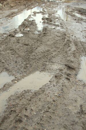 Dirty dirt road with track, wheel marks, brown clay and puddles in Russia.の写真素材