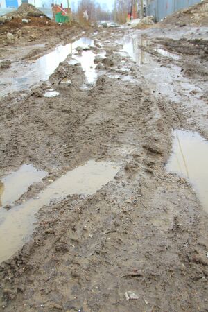 Dirty dirt road with track, wheel marks, brown clay and puddles in Russia.の写真素材