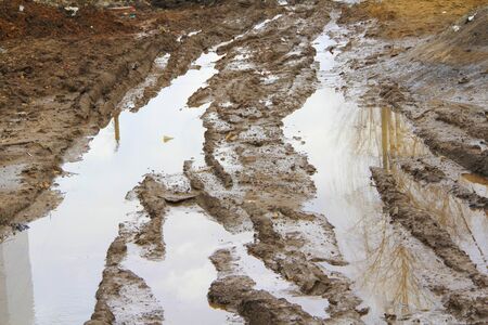 Dirty dirt road with track, wheel marks, brown clay and puddles in Russia.の写真素材