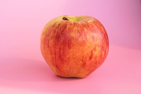 Red yellow apple on a pink background. Juicy ripe beautiful fruit.の写真素材