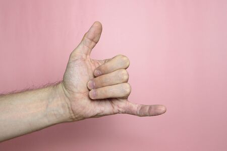 Male hand with fair skin shows a gesture, hand on a light pink background. gesture imitating phone conversation, negotiations, phone call. Stock photo for web and print.の写真素材