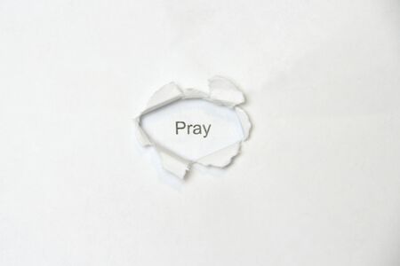 Word pray on white isolated background, the inscription through the wound hole in the paper. Stock photo for web and print with empty space for text and design.の写真素材