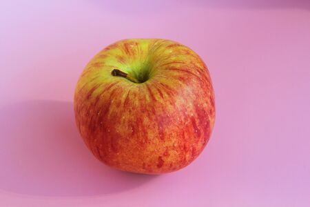 Red yellow apple on a pink background. Juicy ripe beautiful fruit.の写真素材