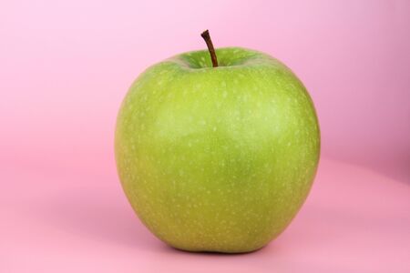 Green yellow apple on a pink background. Juicy ripe beautiful fruit.の写真素材