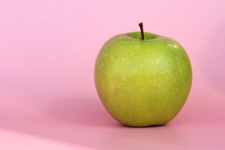 Green yellow apple on a pink background. Juicy ripe beautiful fruit.の写真素材