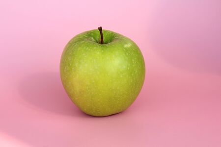 Green yellow apple on a pink background. Juicy ripe beautiful fruit.の写真素材