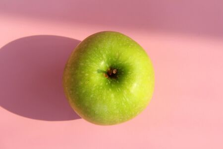Green yellow apple on a pink background. Juicy ripe beautiful fruit.の写真素材