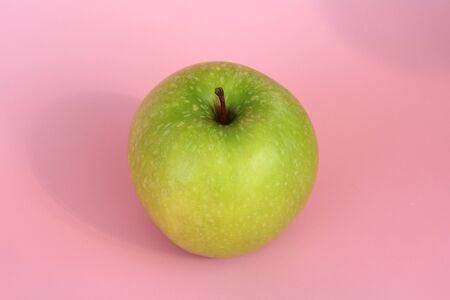 Green yellow apple on a pink background. Juicy ripe beautiful fruit.の写真素材