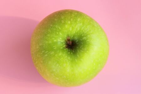 Green yellow apple on a pink background. Juicy ripe beautiful fruit.の写真素材