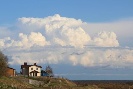 Beautiful landscape with the horizon and with a white house on a hill. Countryside in spring with dry and young green grass. White cumulus clouds against the blue sky. Cottage on the edge of the village next to the railway.の写真素材