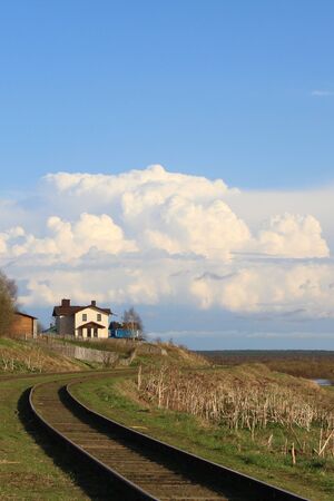 Beautiful landscape with the horizon and with a white house on a hill. Countryside in spring with dry and young green grass. White cumulus clouds against the blue sky. Cottage on the edge of the village next to the railway.の写真素材
