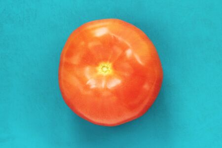 Red juicy ripe tomato on a blue background. Ripe vegetable on a cutting board.の写真素材