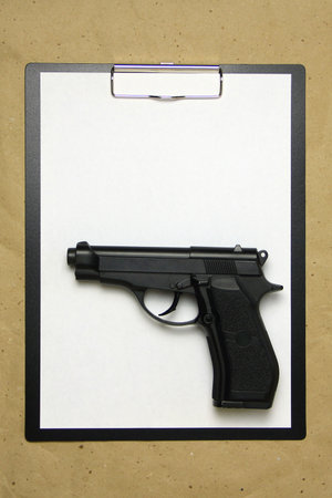 A tablet with a white sheet of A4 format with gun on a beige craft paper. Concept of the legal system, criminal organizations, security services. Stock photo with empty place for your text and design.の写真素材