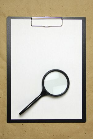 A tablet with a white sheet of A4 format with magnifier on a beige craft paper. Concept of analysis, study, attentive work. Stock photo with empty place for your text and design.の写真素材