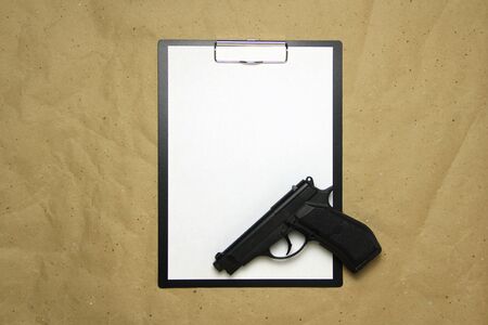 A tablet with a white sheet of A4 format with gun on a beige craft paper. Concept of the legal system, criminal organizations, security services. Stock photo with empty place for your text and design.の写真素材