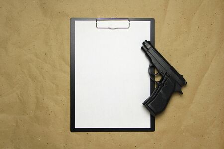 A tablet with a white sheet of A4 format with gun on a beige craft paper. Concept of the legal system, criminal organizations, security services. Stock photo with empty place for your text and design.の写真素材