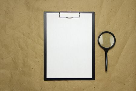 A tablet with a white sheet of A4 format with magnifier on a beige craft paper. Concept of analysis, study, attentive work. Stock photo with empty place for your text and design.の写真素材