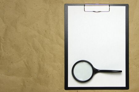 A tablet with a white sheet of A4 format with magnifier on a beige craft paper. Concept of analysis, study, attentive work. Stock photo with empty place for your text and design.の写真素材