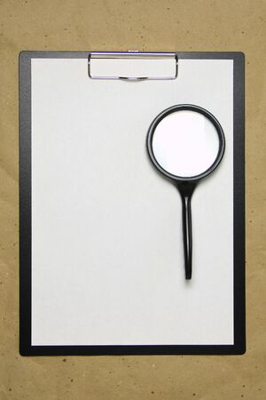 A tablet with a white sheet of A4 format with magnifier on a beige craft paper. Concept of analysis, study, attentive work. Stock photo with empty place for your text and design.の写真素材