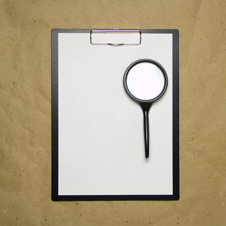A tablet with a white sheet of A4 format with magnifier on a beige craft paper. Concept of analysis, study, attentive work. Stock photo with empty place for your text and design.の写真素材