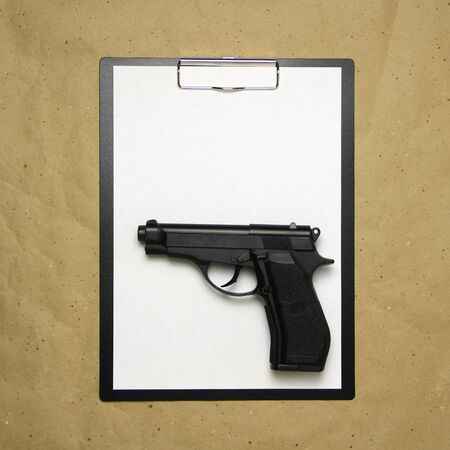 A tablet with a white sheet of A4 format with gun on a beige craft paper. Concept of the legal system, criminal organizations, security services. Stock photo with empty place for your text and design.の写真素材