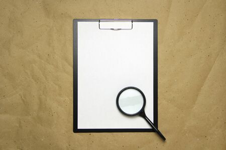 A tablet with a white sheet of A4 format with magnifier on a beige craft paper. Concept of analysis, study, attentive work. Stock photo with empty place for your text and design.の写真素材