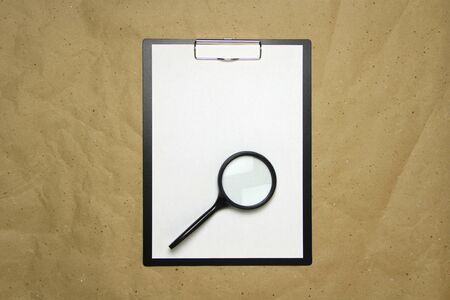 A tablet with a white sheet of A4 format with magnifier on a beige craft paper. Concept of analysis, study, attentive work. Stock photo with empty place for your text and design.の写真素材