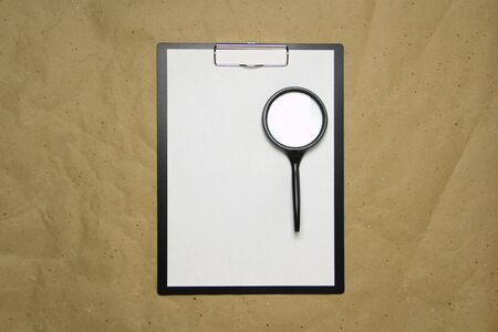 A tablet with a white sheet of A4 format with magnifier on a beige craft paper. Concept of analysis, study, attentive work. Stock photo with empty place for your text and design.の写真素材