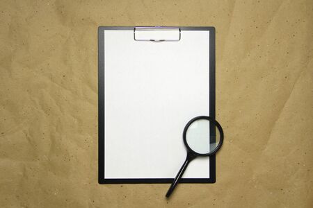 A tablet with a white sheet of A4 format with magnifier on a beige craft paper. Concept of analysis, study, attentive work. Stock photo with empty place for your text and design.の写真素材