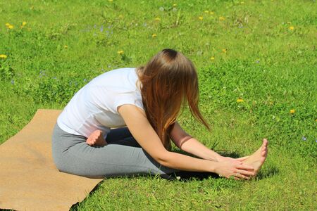 Young woman of European appearance does yoga in summer nature. Woman sitting in mahamudra pose. High quality photo for web and print with empty space for text and design.の写真素材