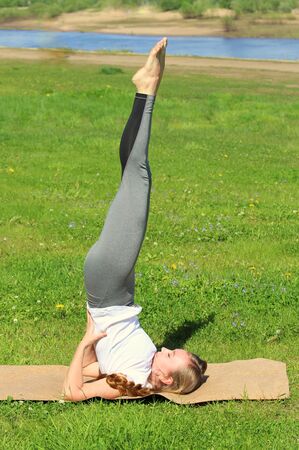 Young woman of European appearance does yoga in summer nature. Girl does a shoulderstand, salamba sarvangasana. High quality photo for web and print with empty space for text and design.の写真素材