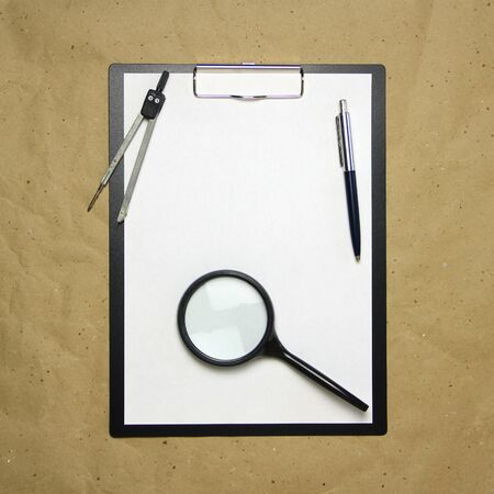 A tablet with a white sheet of A4 format with magnifier, pen and divider on a beige craft paper. Concept of analysis, study, attentive work. Stock photo with empty place for your text and design.の写真素材
