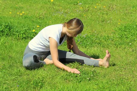 Young woman of European appearance does yoga in summer nature. Woman sitting in mahamudra pose. High quality photo for web and print with empty space for text and design.の写真素材