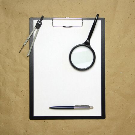 A tablet with a white sheet of A4 format with magnifier, pen and divider on a beige craft paper. Concept of analysis, study, attentive work. Stock photo with empty place for your text and design.の写真素材