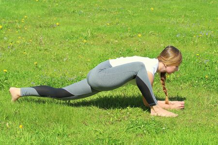 Young woman of European appearance does yoga in summer nature. Woman standing in lunge pose, banarasana. High quality photo for web and print with empty space for text and design.の写真素材