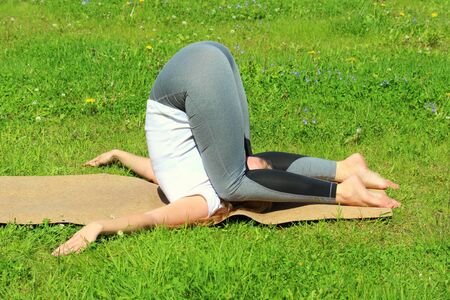 Young woman of European appearance does yoga in summer nature. Woman lies in perfect plow pose, maha halasana. High quality photo for web and print with empty space for text and design.の写真素材