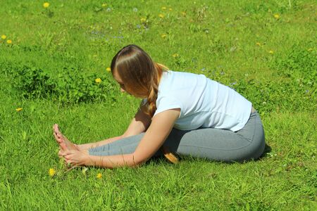 Young woman of European appearance does yoga in summer nature. Woman seated forward bend in pose paschimottanasana. High quality photo for web and print with empty space for text and design.の写真素材