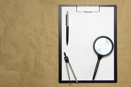 A tablet with a white sheet of A4 format with magnifier, pen and divider on a beige craft paper. Concept of analysis, study, attentive work. Stock photo with empty place for your text and design.の写真素材