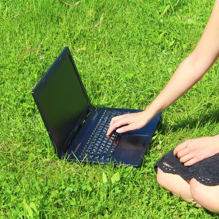 The laptop is on the green grass, the girl works at the computer on the lawn. The man's hand is on the keyboard.の写真素材