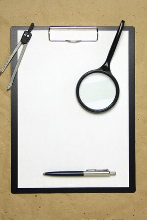 A tablet with a white sheet of A4 format with magnifier, pen and divider on a beige craft paper. Concept of analysis, study, attentive work. Stock photo with empty place for your text and design.の写真素材