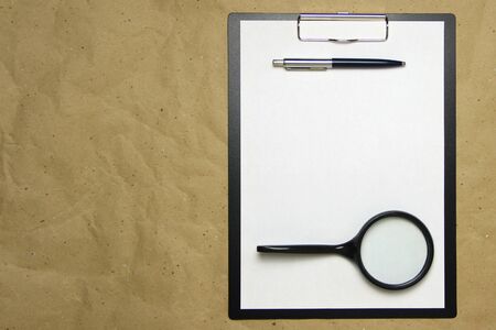 A tablet with a white sheet of A4 format with magnifier, pen and magnifier on a beige craft paper. Concept of analysis, study, attentive work. Stock photo with empty place for your text and design.の写真素材